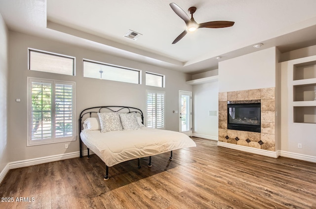 bedroom featuring dark wood-type flooring, ceiling fan, a tray ceiling, and a tile fireplace