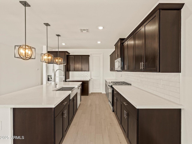 kitchen with stainless steel appliances, sink, light wood-type flooring, decorative backsplash, and hanging light fixtures