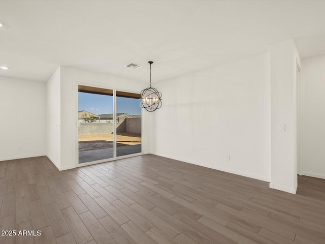 empty room featuring an inviting chandelier and hardwood / wood-style flooring