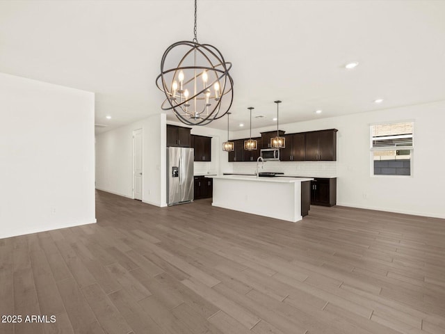 kitchen featuring hardwood / wood-style floors, appliances with stainless steel finishes, an island with sink, a notable chandelier, and pendant lighting