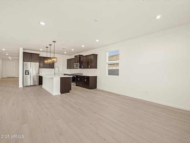 kitchen featuring pendant lighting, an island with sink, backsplash, appliances with stainless steel finishes, and sink