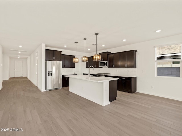 kitchen featuring stainless steel appliances, light hardwood / wood-style flooring, decorative light fixtures, and a center island with sink