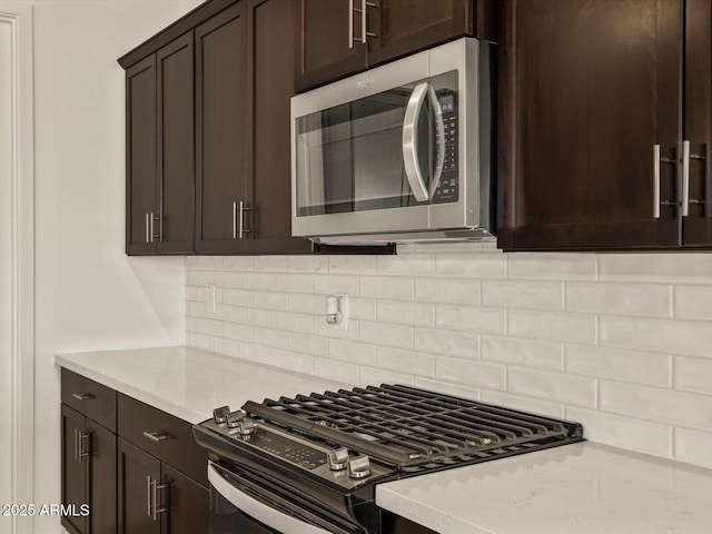 kitchen featuring stainless steel appliances, decorative backsplash, dark brown cabinetry, and light stone countertops