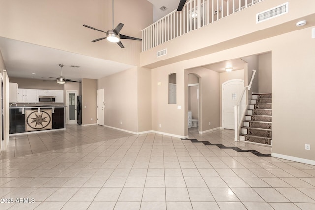 7029 S Golfside Ln, Phoenix, AZ 85042 - unfurnished living room with a ceiling fan, light tile patterned flooring, arched walkways, stairway, and a towering ceiling