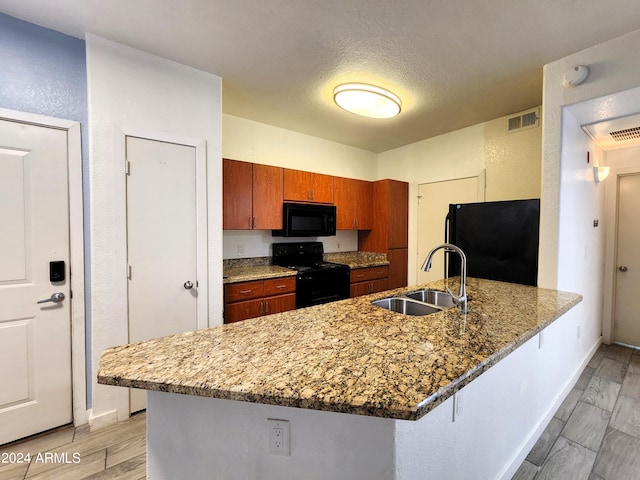 kitchen featuring sink, a textured ceiling, light hardwood / wood-style flooring, black appliances, and a breakfast bar area