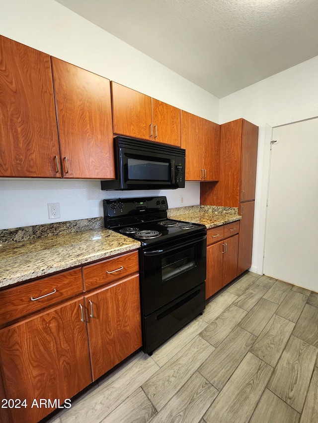 kitchen featuring light stone countertops, light wood-type flooring, black appliances, and a textured ceiling