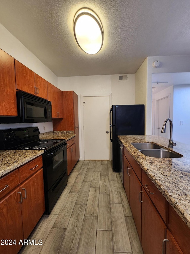 kitchen with light stone counters, a textured ceiling, black appliances, light hardwood / wood-style flooring, and sink