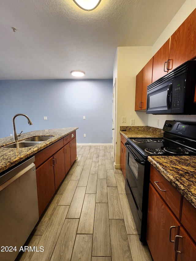 kitchen featuring dark stone counters, a textured ceiling, light hardwood / wood-style floors, sink, and black appliances