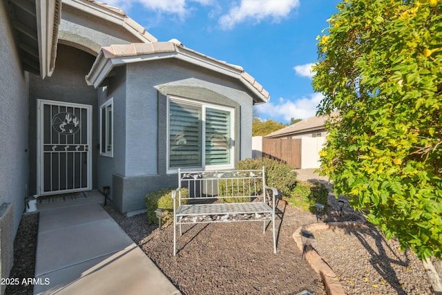 entrance to property featuring fence and stucco siding