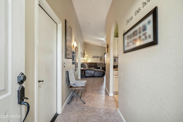 hallway with arched walkways, baseboards, and light tile patterned floors