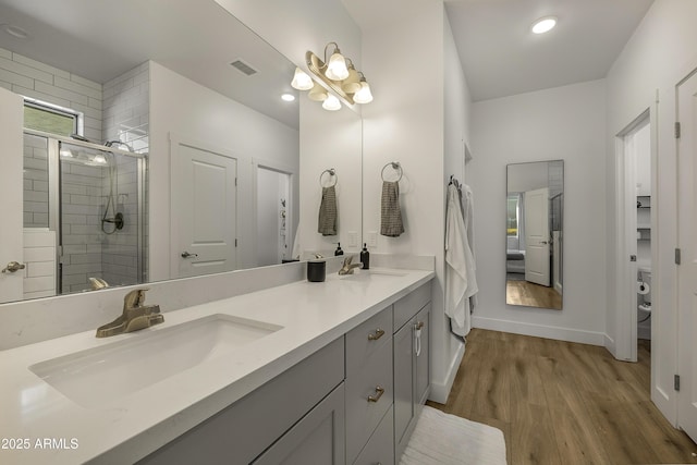 bathroom featuring a sink, double vanity, a shower stall, wood finished floors, and visible vents