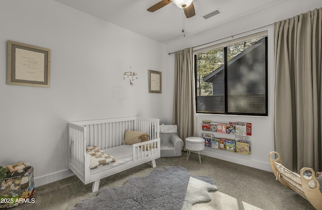 carpeted bedroom with a crib, baseboards, a ceiling fan, and visible vents