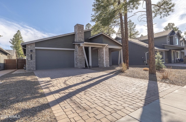 mid-century home with decorative driveway, fence, a chimney, and a garage