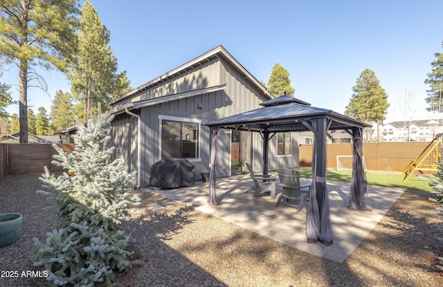 rear view of house featuring a patio, a fenced backyard, board and batten siding, a playground, and a gazebo
