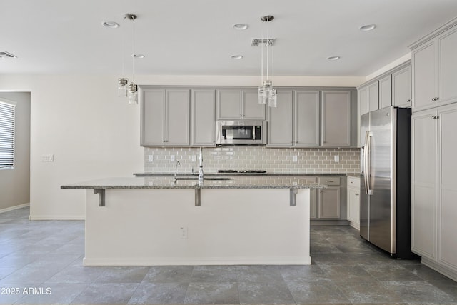 kitchen featuring an island with sink, appliances with stainless steel finishes, a breakfast bar, and decorative light fixtures