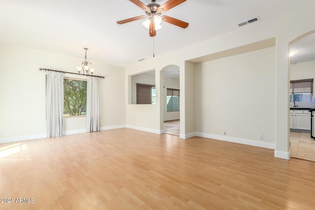 unfurnished living room with ceiling fan with notable chandelier and light hardwood / wood-style floors