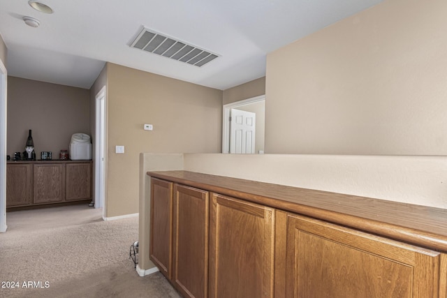 hallway with visible vents, light carpet, and baseboards