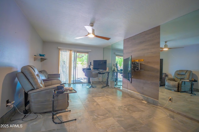 living area featuring a ceiling fan, wood walls, and baseboards