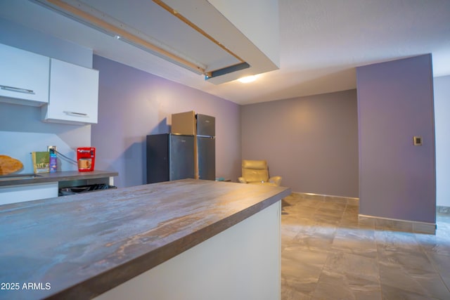 kitchen featuring freestanding refrigerator, white cabinetry, and baseboards