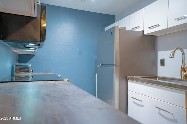 kitchen featuring a sink, freestanding refrigerator, and white cabinetry