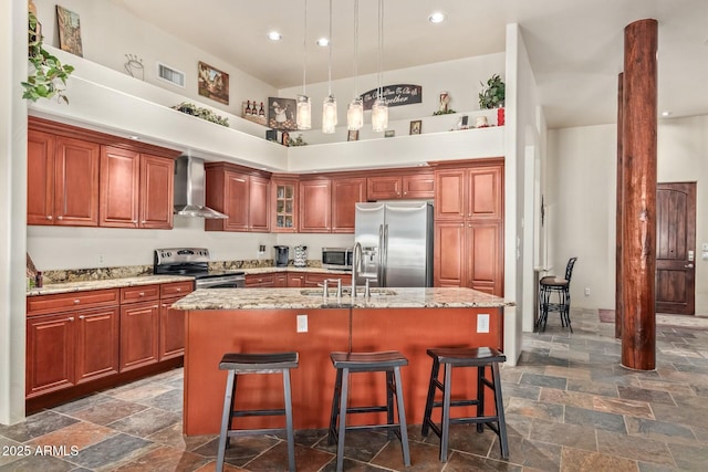 kitchen featuring wall chimney range hood, a breakfast bar, stainless steel appliances, light stone counters, and a center island with sink