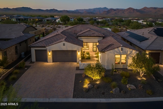 mediterranean / spanish home featuring decorative driveway, a tile roof, stucco siding, a mountain view, and a garage