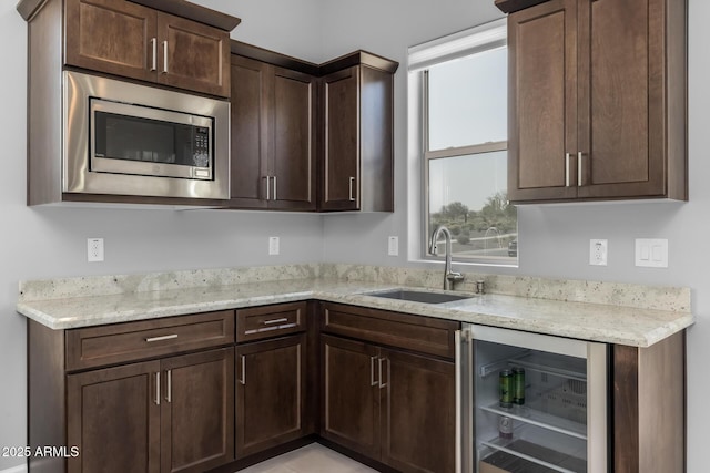 kitchen with light stone counters, wine cooler, dark brown cabinetry, a sink, and stainless steel microwave