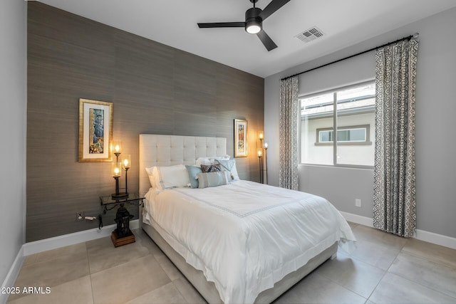 bedroom featuring light tile patterned floors, an accent wall, a ceiling fan, visible vents, and baseboards