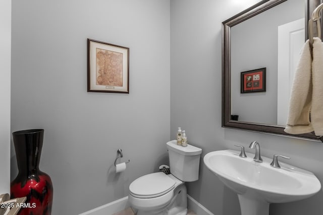 half bathroom featuring toilet, baseboards, and a sink