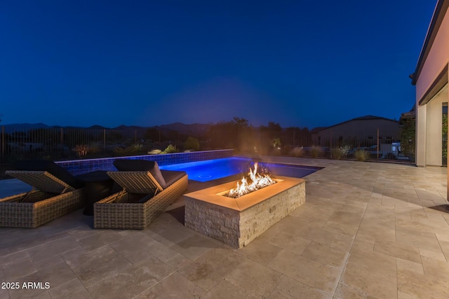 pool at night with an outdoor fire pit, an outdoor pool, and a patio