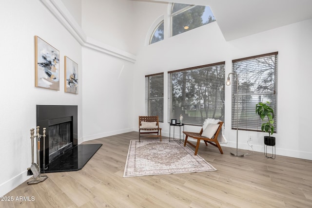 sitting room with a fireplace with raised hearth, a high ceiling, wood finished floors, and baseboards