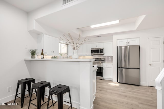 kitchen featuring a skylight, light wood finished floors, a breakfast bar area, appliances with stainless steel finishes, and white cabinetry