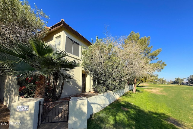 view of home's exterior with a fenced front yard, stucco siding, a lawn, a gate, and a tiled roof