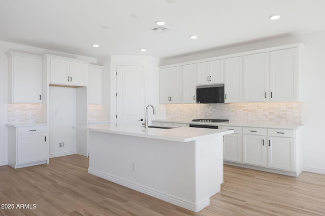 kitchen with white cabinetry, light hardwood / wood-style floors, sink, and a center island with sink