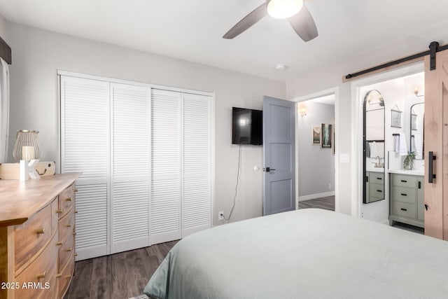 bedroom with ceiling fan, a barn door, connected bathroom, dark hardwood / wood-style floors, and a closet