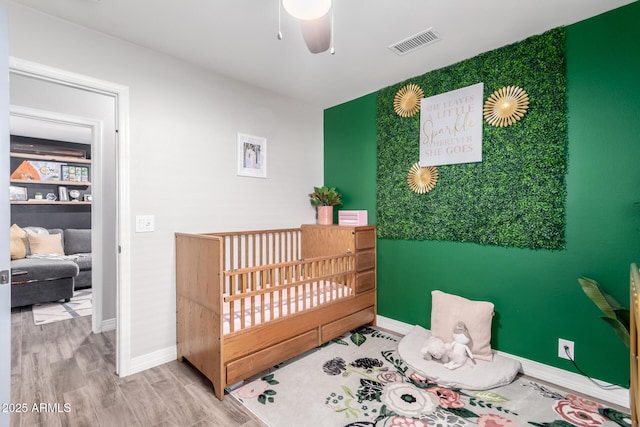 bedroom with ceiling fan, a nursery area, and wood-type flooring