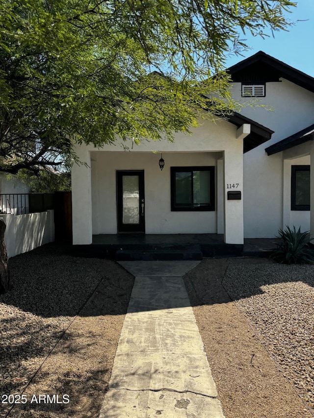 doorway to property with stucco siding, covered porch, and fence