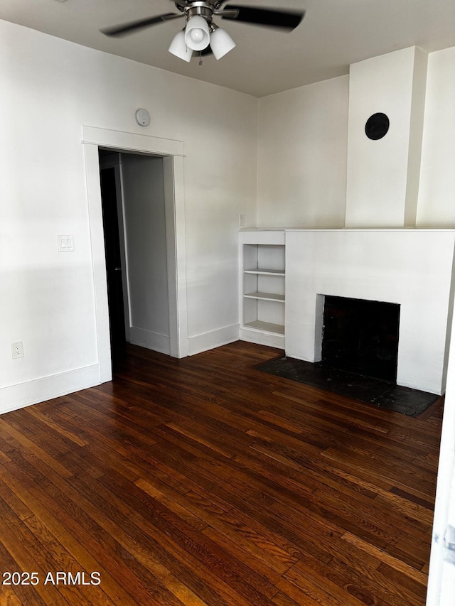 unfurnished living room with dark wood-style flooring, a brick fireplace, baseboards, and ceiling fan