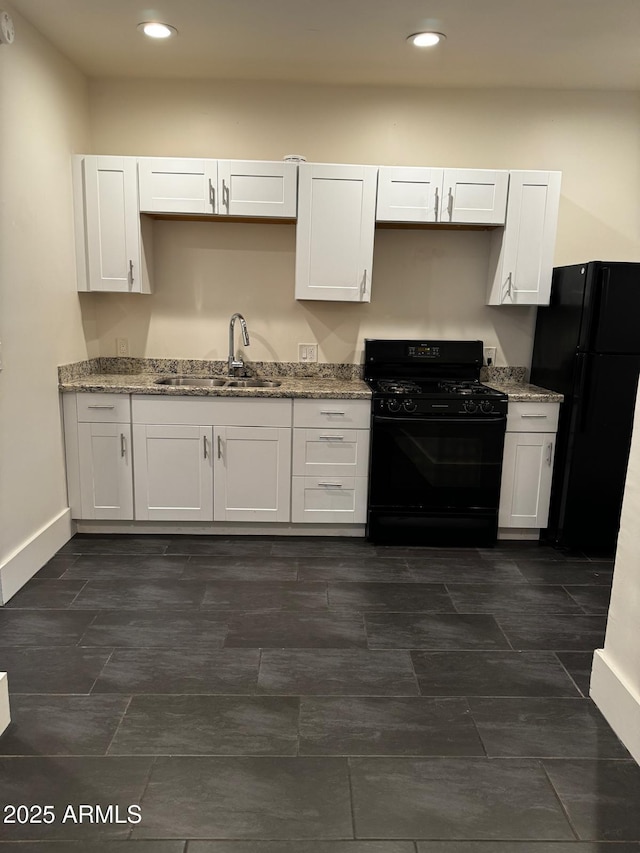 kitchen featuring baseboards, black appliances, white cabinets, and a sink