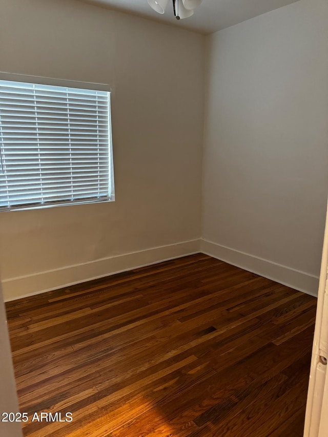 empty room featuring baseboards, a notable chandelier, and dark wood finished floors