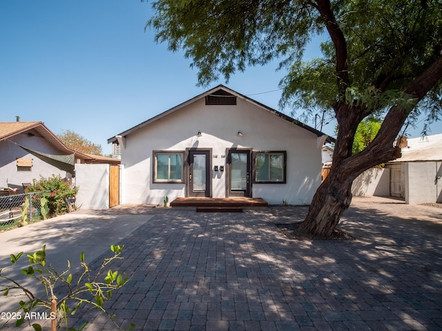 bungalow with decorative driveway, stucco siding, and fence
