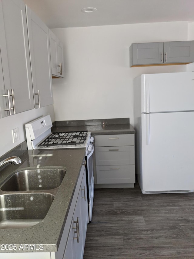 kitchen featuring white appliances, dark stone counters, a sink, and dark wood-type flooring