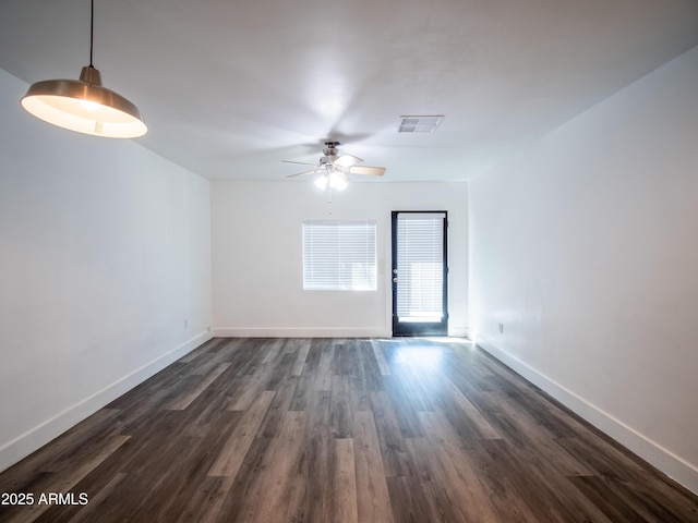 empty room featuring dark wood-style flooring, baseboards, a ceiling fan, and visible vents