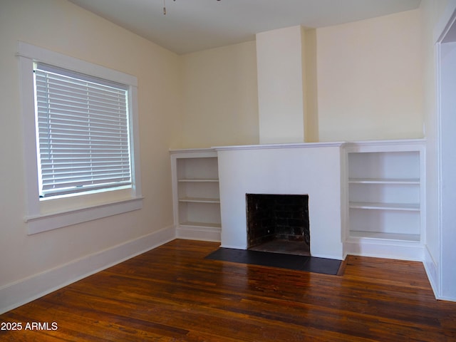unfurnished living room with baseboards, built in shelves, a fireplace with flush hearth, and wood finished floors