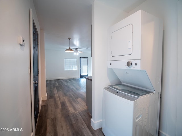 laundry room featuring laundry area, stacked washer / drying machine, dark wood-type flooring, ceiling fan, and baseboards