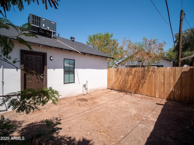 rear view of house with stucco siding, fence, central air condition unit, a patio area, and roof with shingles