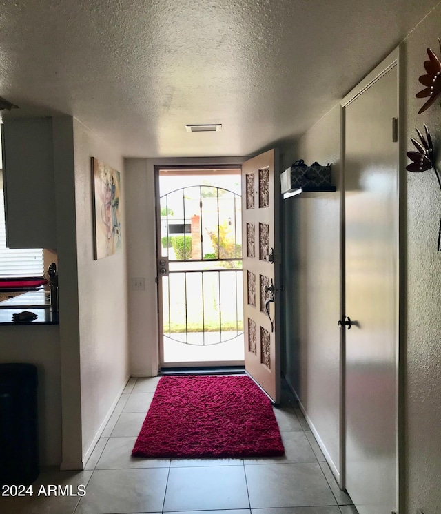 doorway to outside with a textured ceiling and light tile patterned floors