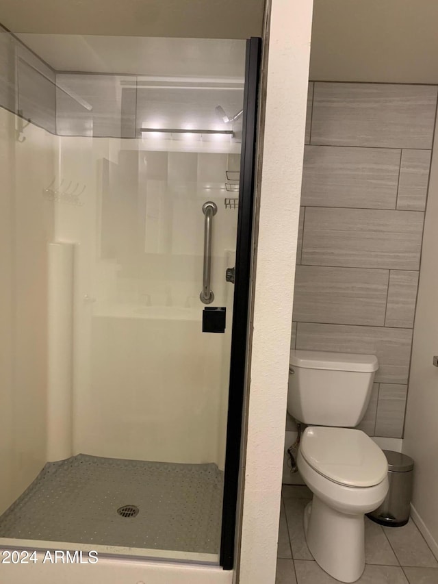 bathroom featuring tile patterned floors, toilet, tile walls, and a shower