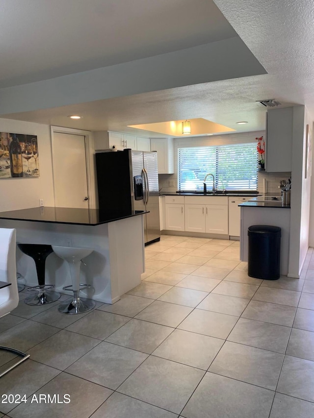 kitchen with sink, white cabinetry, stainless steel fridge with ice dispenser, light tile patterned floors, and backsplash