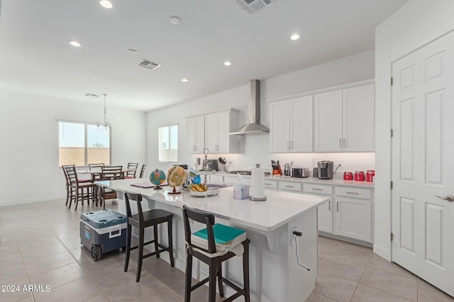 kitchen featuring wall chimney exhaust hood, a kitchen breakfast bar, a center island with sink, and white cabinetry